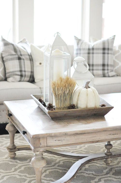 a wooden tray with wheat, white candle lanterns and a faux white pumpkin for fall living room decor