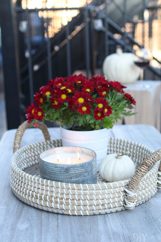 a woven tray with a white pumpkin, an oversized candle in a metal tin and pitted burgundy blooms for a chic and bold look