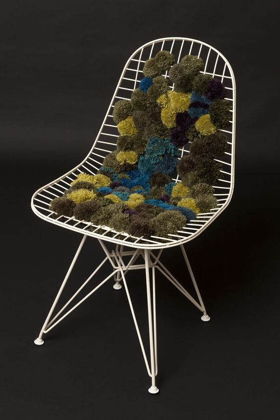 an Eames chair with a metal frame and green, blue and yellow pompoms that form a soft seat and back