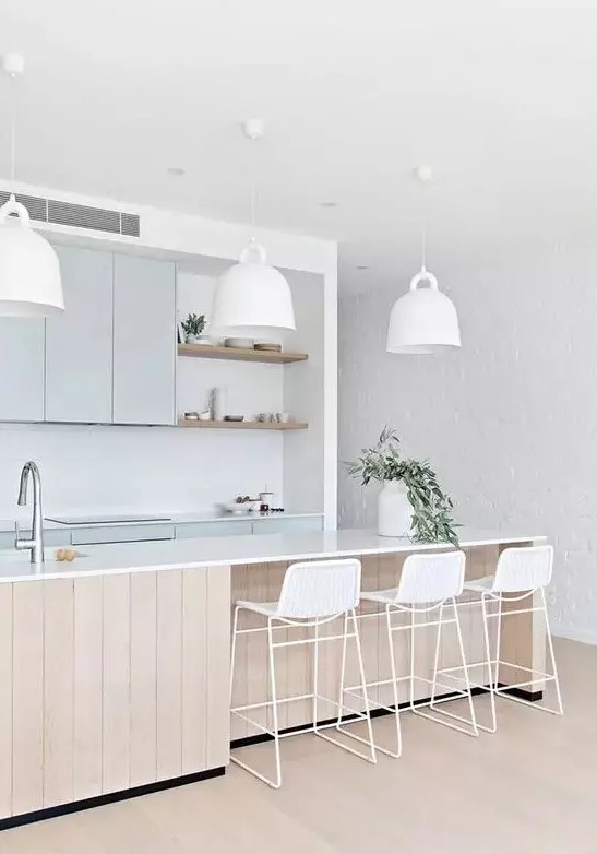 an airy coastal kitchen with light blue cabinetry, a large wooden kitchen island, white mug-shaped pendant lamps, white wicker stools
