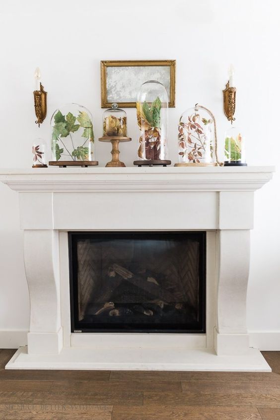 an elegant fall mantel with dried leaves and greenery in a variety of cloches