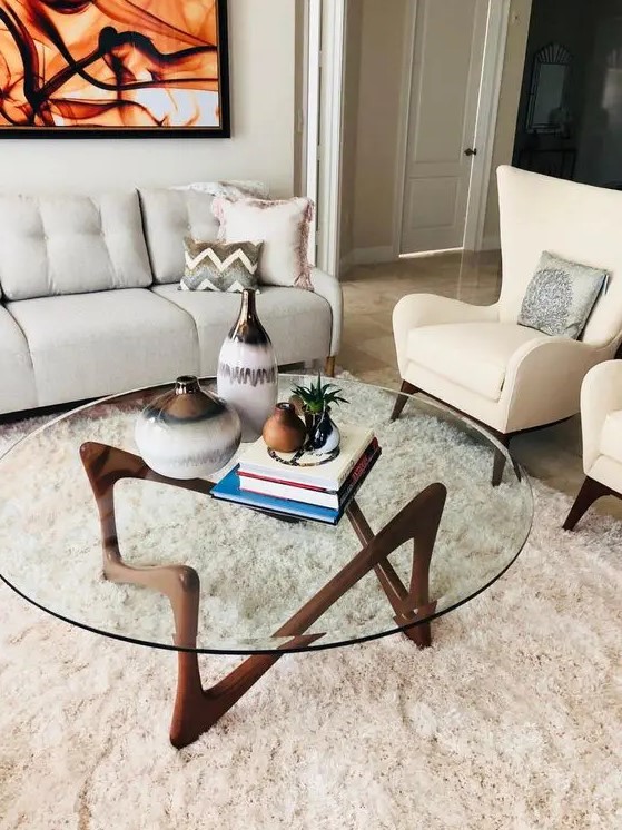 An eye catchy mid century modern coffee table with a round clear glass tabletop and a quirky dark stained wooden base is wow