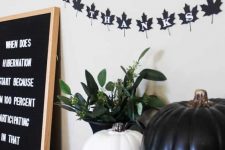 a black and white pumpkin, a black leaf bunting, a black sign and greenery in a black vase for chic and lovely Halloween decor