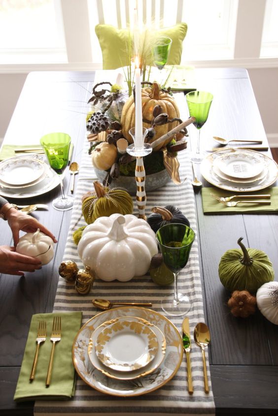 a bold Thanksgiving tablescape with a striped runner, green napkins and placemats, green glasses and faux pumpkins
