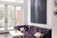 a bold modern living room with a low purple sofa and a large pouf, a white table and an oversized black artwork