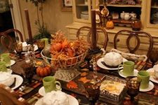 a bold vintage Thanksgiving tablescape with plaid placemats, green mugs, brown candles, a bold pumpkin and dried leaf centerpiece