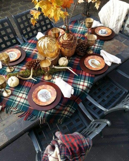 a bright Thanksgiving table with antlers, pumpkins, pinecones, a plaid tablecloth and a fall leaf arrangement