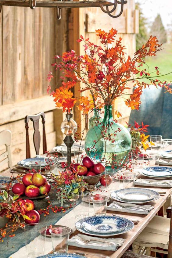 a bright and natural Thanksgiving tablescape with bold apple arrangements, berries, leaves and a bright fall leaf arrangement in a large vase