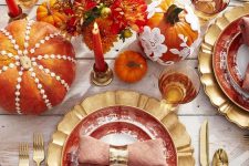 a bright and whisy Thanksgiving tablescape with gold chargers, cutlery, colorful pumpkins and floral arrangements, bold candles