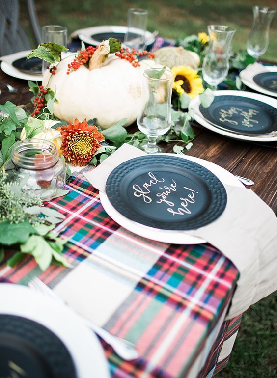 a bright fall tablescape with plaid touches, a large pumpkin, bright blooms and greenery and candles in jars