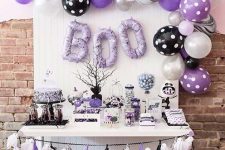 a catchy Halloween sweets table in black, white and purple, with a balloon garland and balloons letters plus a ghost bunting and some paper balls