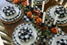a chic black and white Thanksgiving tablescape with buffalo check plates, pumpkins and a runner, faux pumpkins and tall candles