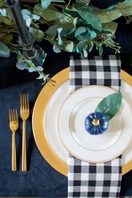 a chic farmhouse Thanksgiving tablescape with a navy tablecloth, plaid napkins, a navy pumpkin, a gold charger and gold cutlery