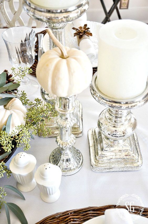 a chic neutral Thanksgiving tablescape with mini pumpkins, large candles, mercury glass candleholders and some greenery