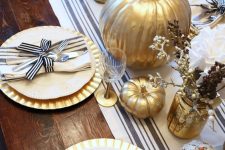 a chic rustic Thanksgiving tablescape with a striped runner, gold chargers, striped napkins, gilded pumpkins and faux branches