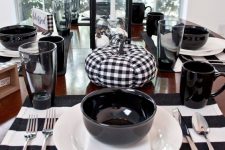 a cool black and white Thanksgiving table with striped placemats, black bowls and mugs, buffalo check pumpkins