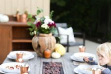 a cool wooden table with a wooden bowl with pumpkins and gourds, copper glasses and ugs and a floral centerpiece in a pumpkin