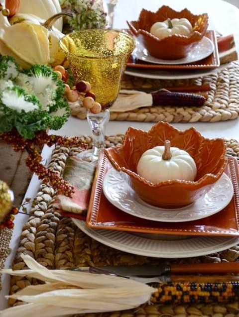 a cozy rustic Thanksgiving tablescape with woven placemats, white and orange plates, white pumpkins, corn cobs and veggies