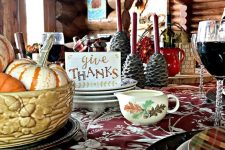 a cozy vintage-inspired Thanksgiving tablescape with a floral tablecloth, printed plates, a floral milk jug, pinecone candleholders and a bowl with pumpkins