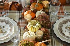a cozy vintage rustic Thanksgiving tablescape with a plaid tablecloth, printed plates, natural pumpkins, leaves and hydrangeas, candles and nuts