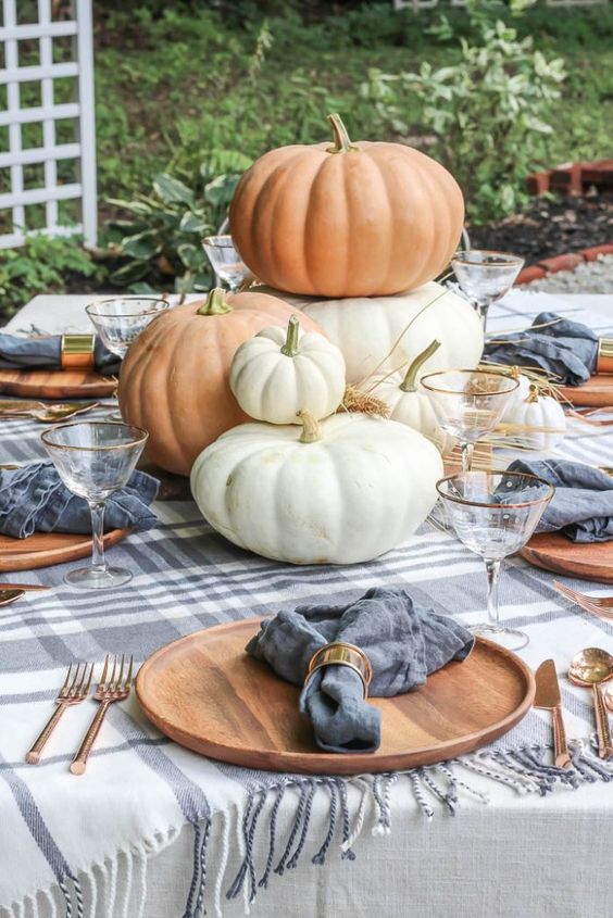 a cute and neutral tablescape with plaid linens, fresh pumpkins stacked and some hay on the table