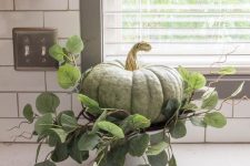 a green heirloom pumpkin with greenery on a stand for rustic Thanksgiving decor