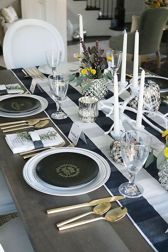 a lovely black and white Thanksgiving tablescape with a buffalo check runner, white candles, black plates and gold cutlery