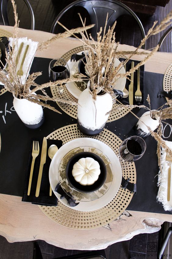 a modern and exquisite Thanksgiving tablescape with gold chargers and cutlery, black linens and wheat in black and white vases