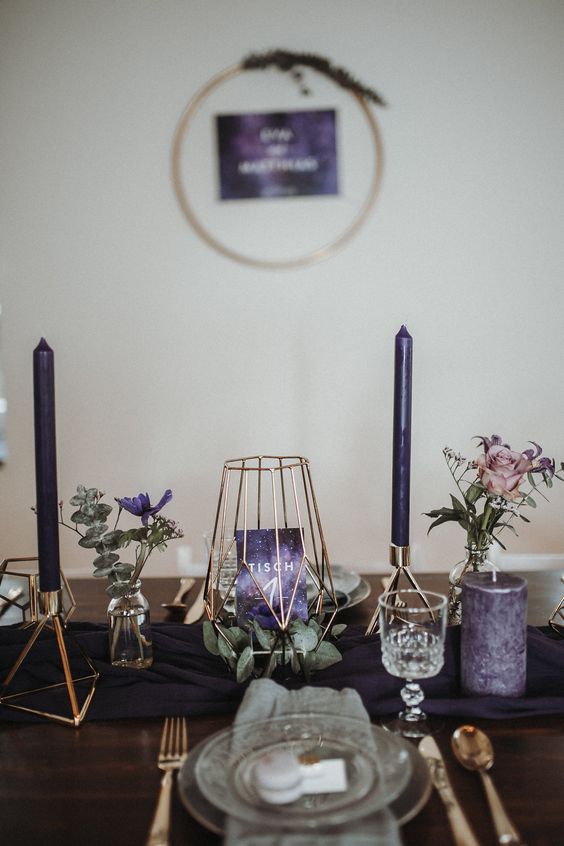 a modern and fresh purple Thanksgiving tablescape with purple candles, blooms and a table number, a deep purple table runner and gold cutlery