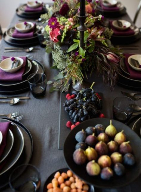 a moody Thanksgiving tablescape with a grey tablecloth, purple napkins, black plates and candles, black bowls with food