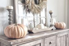 a neutral rustic Thanksgiving console table with a corn husk wreath, large and small pumpkins and candles