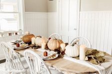 a neutral rustic vintage Thanksgiving table with neutral pumpkins, candles, leaves and simple white porcelain