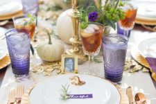 a refined gold and purple Thanksgiving tablescape with gold cutleyr, chargers and candlesticks, white pumpkins, greenery, purple glasses and napkins