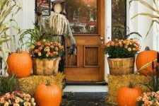a rustic Halloween porch with a scarecrow, pumpkins, hay and bright blooms in wooden baskets