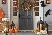 a rustic Halloween porch with paper blackbirds, a fall leaf and veggie garland and wreath, laser cut pumpkins, laeaves and candle lanterns
