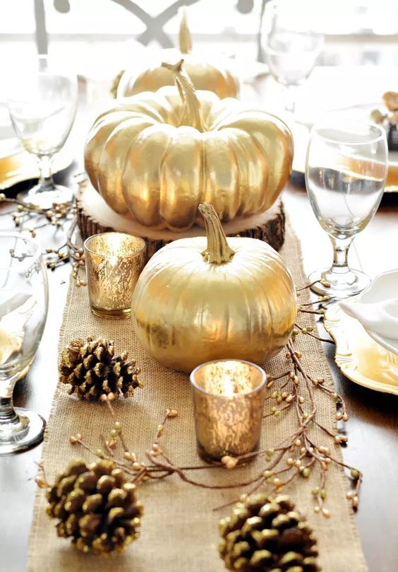 a rustic Thanksgiving tablescape with a burlap runner, berries on branches, gilded pinecones and creatively shaped plates