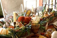a rustic vintage Thanksgiving tablescape with a large bowl centerpiece with pumpkins, greenery, candles and feathers, plaid placemats, printed plates