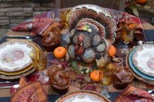 a rustic vintage Thanksgiving tablescape with a plaid tablecloth, bright napkins, a large turkey, colored glasses and mini pumpkins