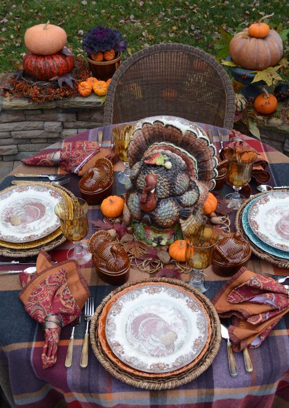 a rustic vintage Thanksgiving tablescape with a plaid tablecloth, bright napkins, a large turkey, colored glasses and mini pumpkins