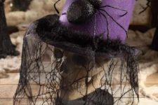 a skull dressed into a purple hat with a large spider and a lace spiderweb veil is a creative old-fashioned decoration for Halloween