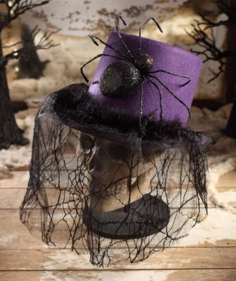 A skull dressed into a purple hat with a large spider and a lace spiderweb veil is a creative old fashioned decoration for Halloween