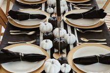 a stylish black and white Thanksgiving tablescape with a striped runner, gold chargers, gold candleholders, black and white pumpkins and black napkins