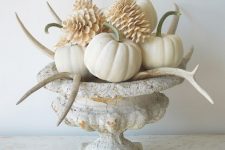 a stylish vintage Thanksgiving centerpiece of a vintage urn, bleached pinecones, antlers and pumpkins is chic
