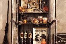 a vintage Halloween storage unit in black, with pumpkins, gourds, candles, signs and a broom by its side is a lovely idea for your party