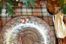 a vintage rustic Thanksgiving table with a plaid tablecloth, a printed plate, leaves, acorns, pumpkins and candles