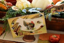a vintage rustic centerpiece of a wooden box with greenery, gourds, pumpkins and feathers and a vintage card