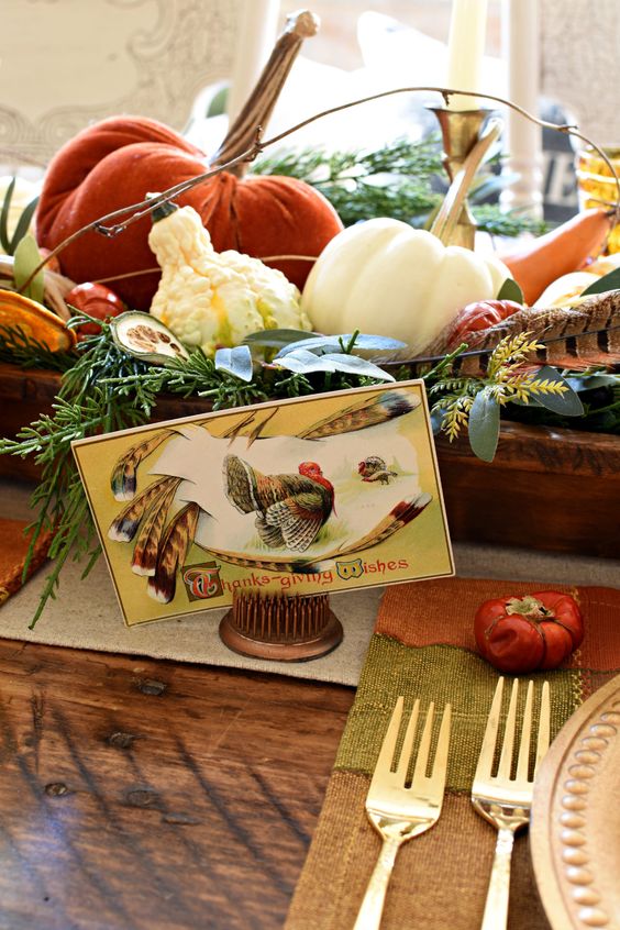 a vintage rustic centerpiece of a wooden box with greenery, gourds, pumpkins and feathers and a vintage card