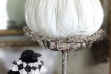 a white pumpkin on a stand, with a black spider and a crown plus green leaves and hay is a cool decoration for Halloween