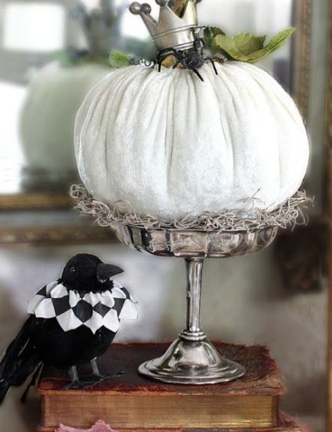 a white pumpkin on a stand, with a black spider and a crown plus green leaves and hay is a cool decoration for Halloween