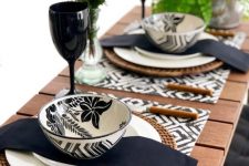 an eye-catchy black and white Thanksgiving tablescape with printed placemats, printed bowls, black napkins, greenery and black glasses